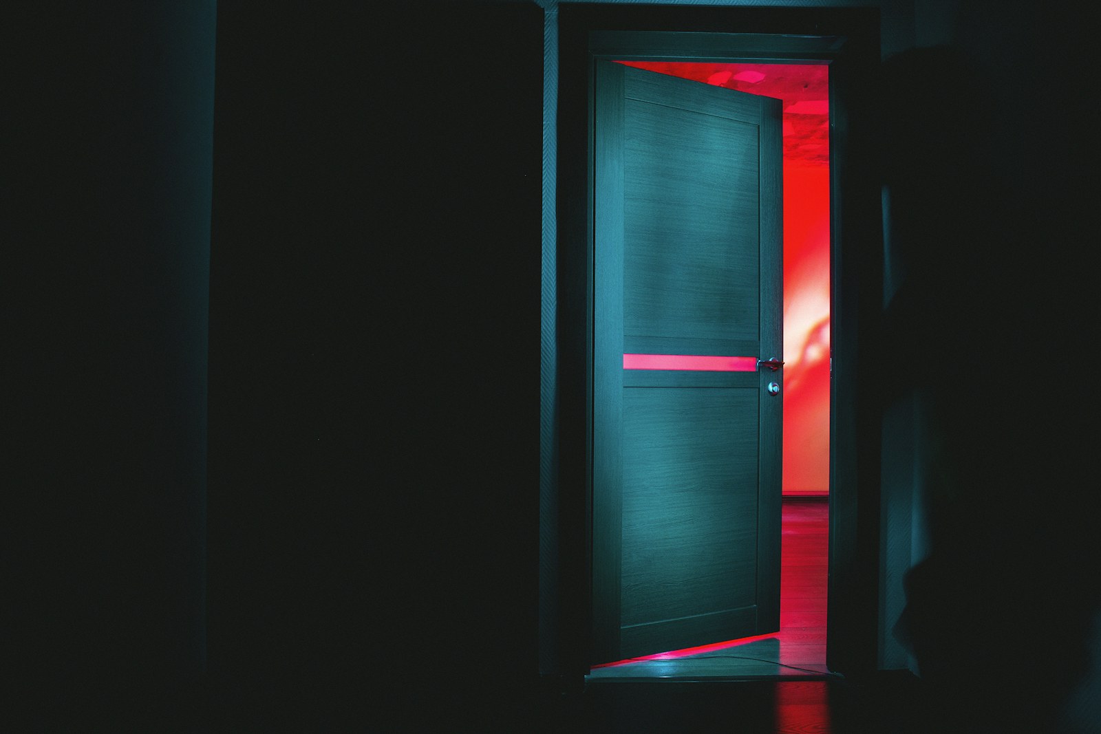 A partially open door revealing a bright red room in a dark space