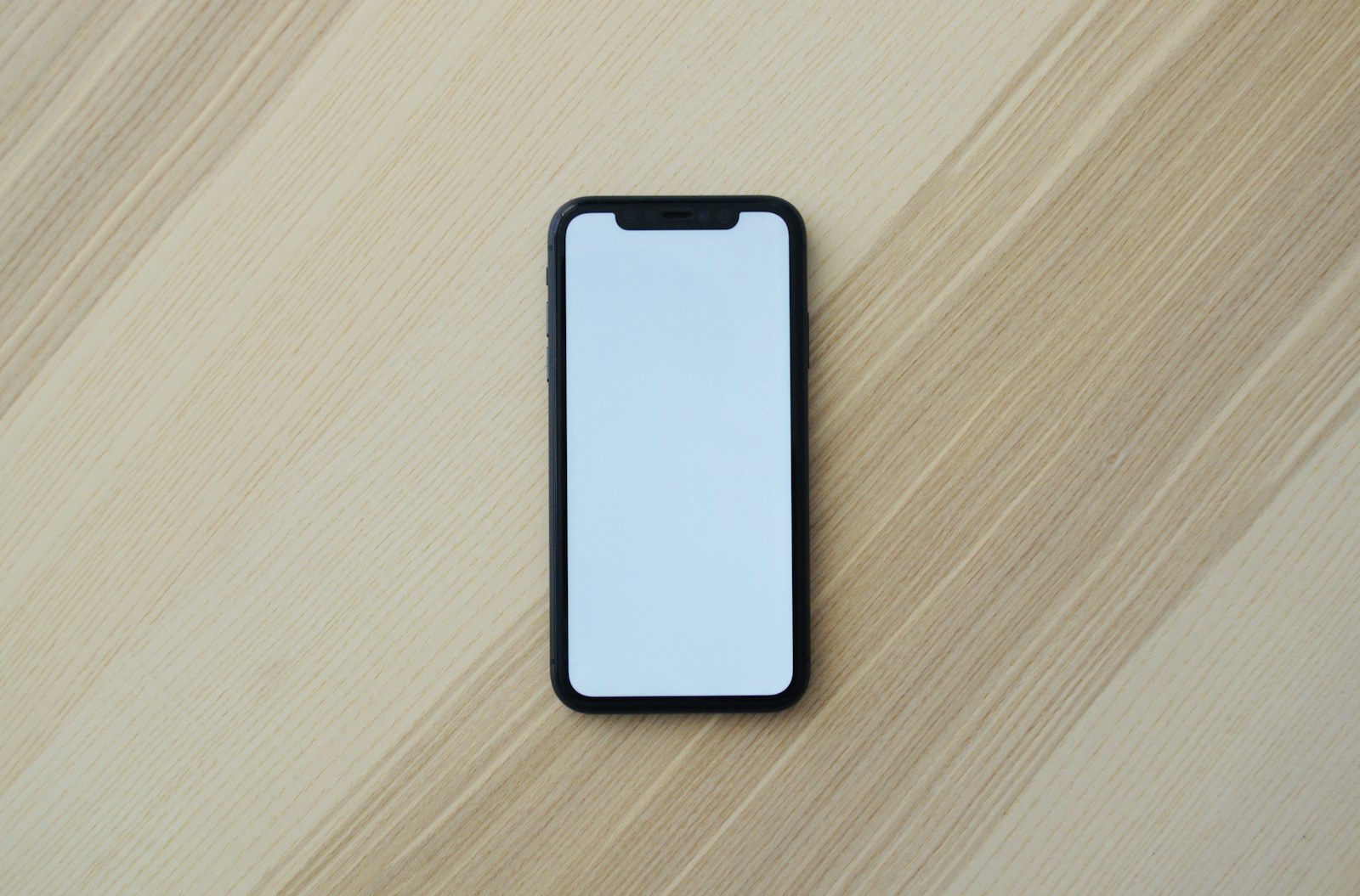 A black smartphone with a blank white screen on a light wooden surface