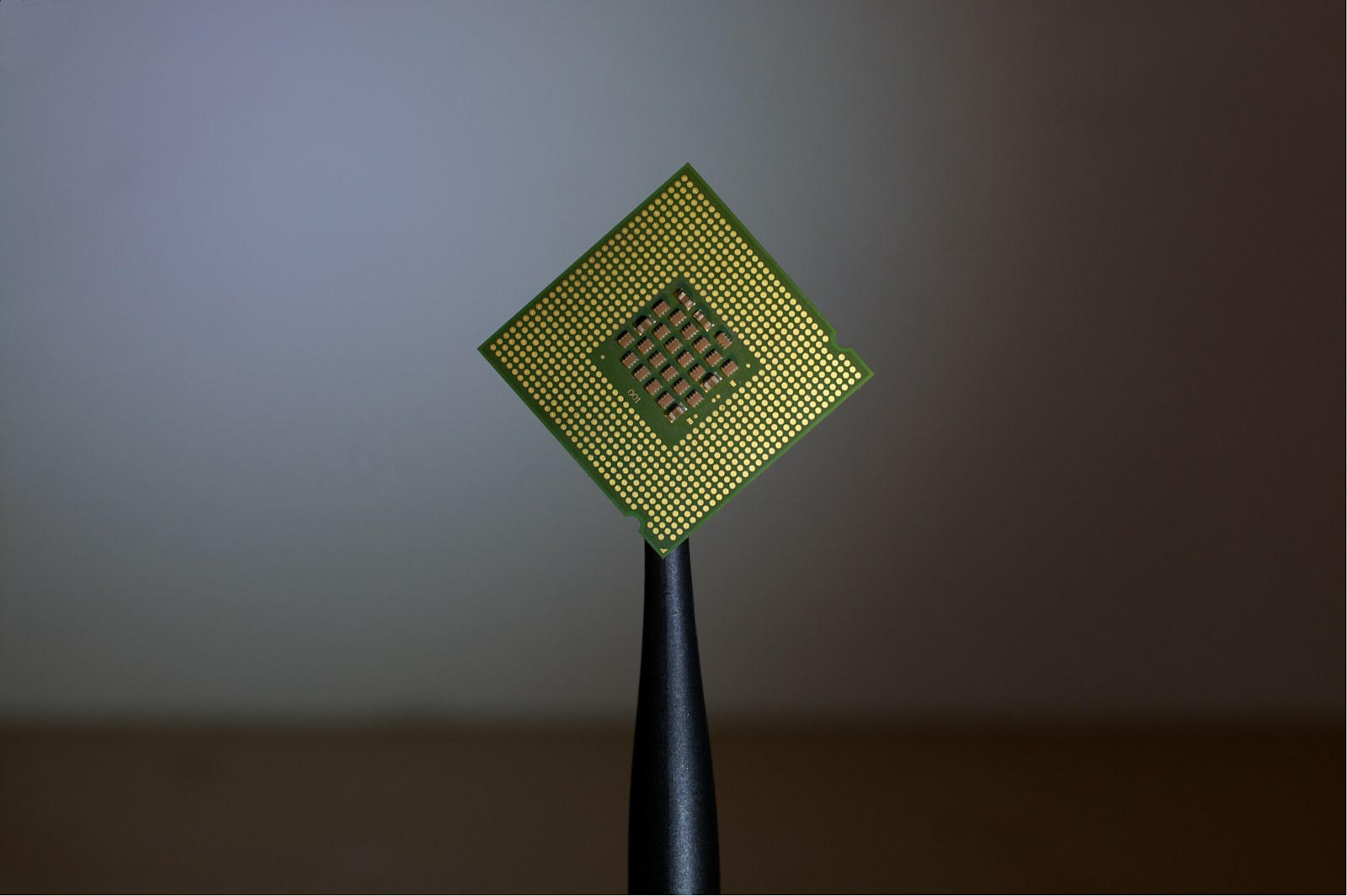 A computer processor held by black tweezers against a neutral background