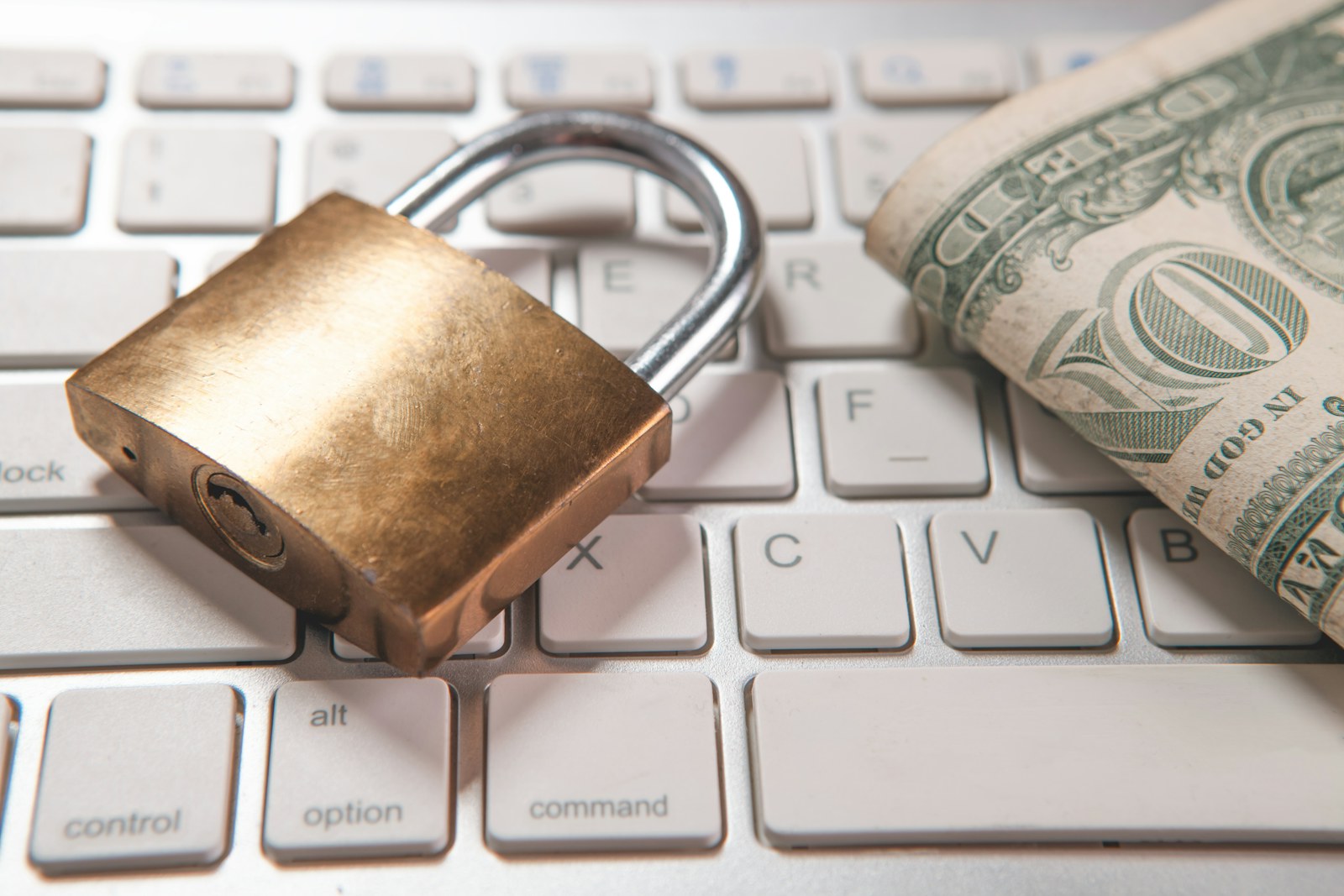 A padlock and dollar bills rest on a computer keyboard