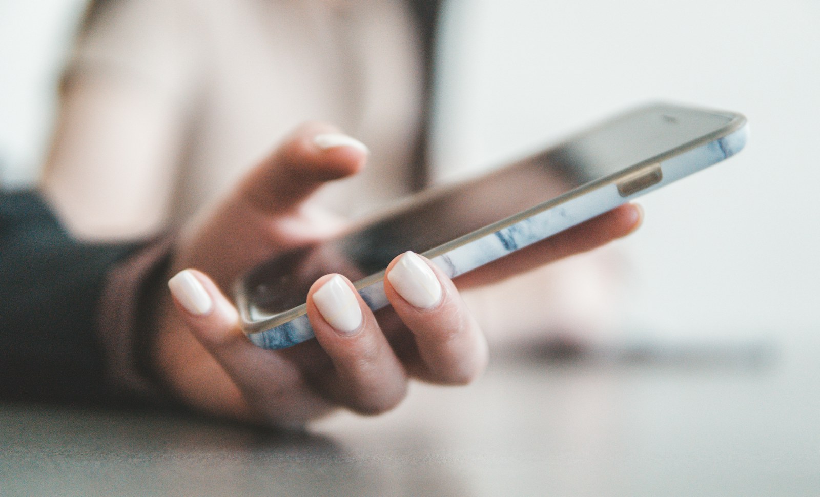 A person holding a smartphone with a marble pattern case in a bright room