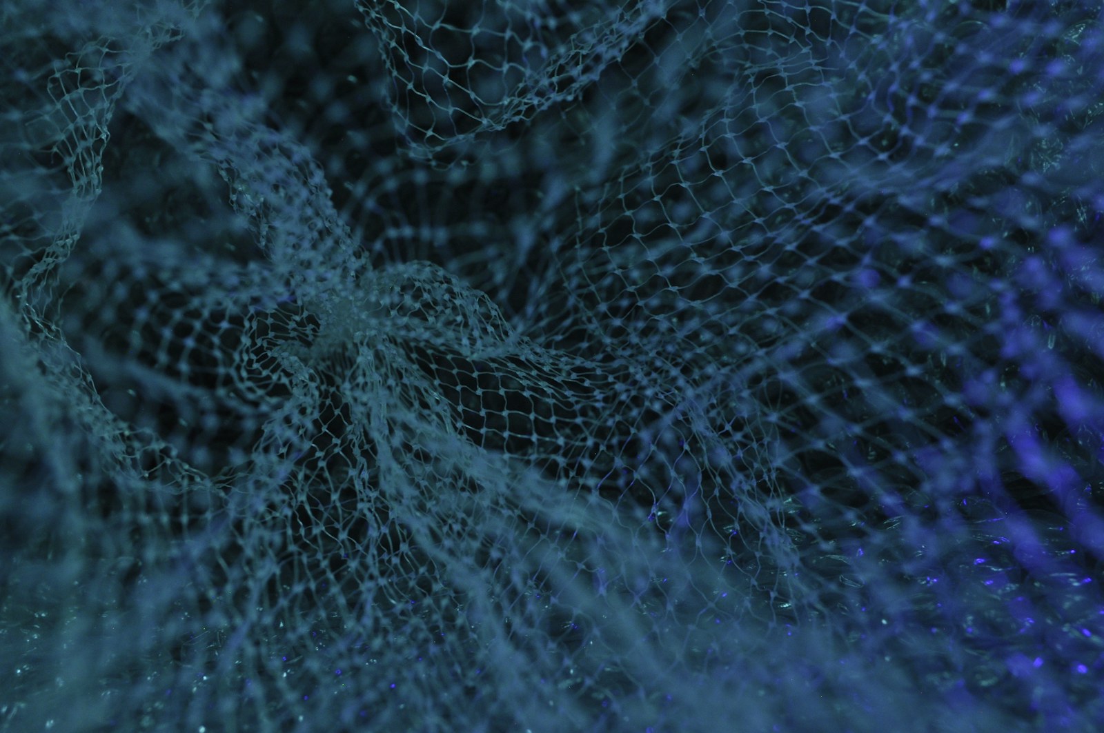 A fine white mesh fabric draped over a dark surface under blue light