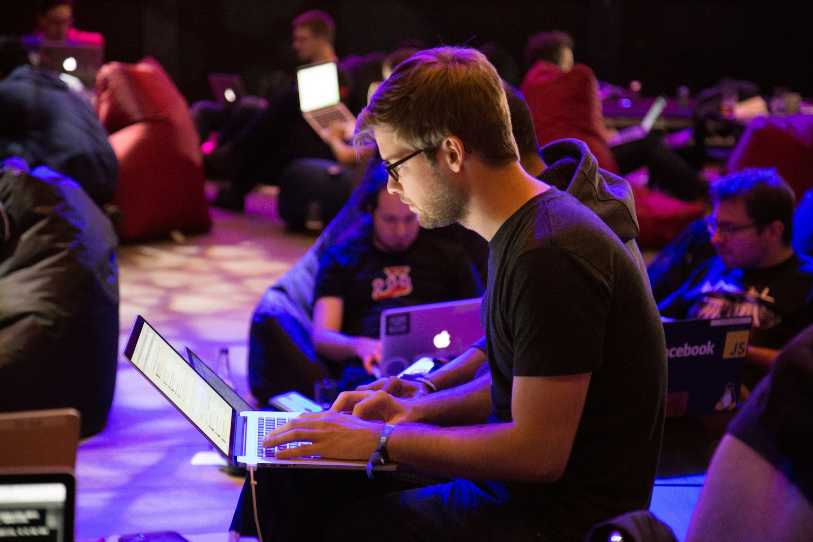 A man in glasses typing on a laptop in a dimly lit workspace