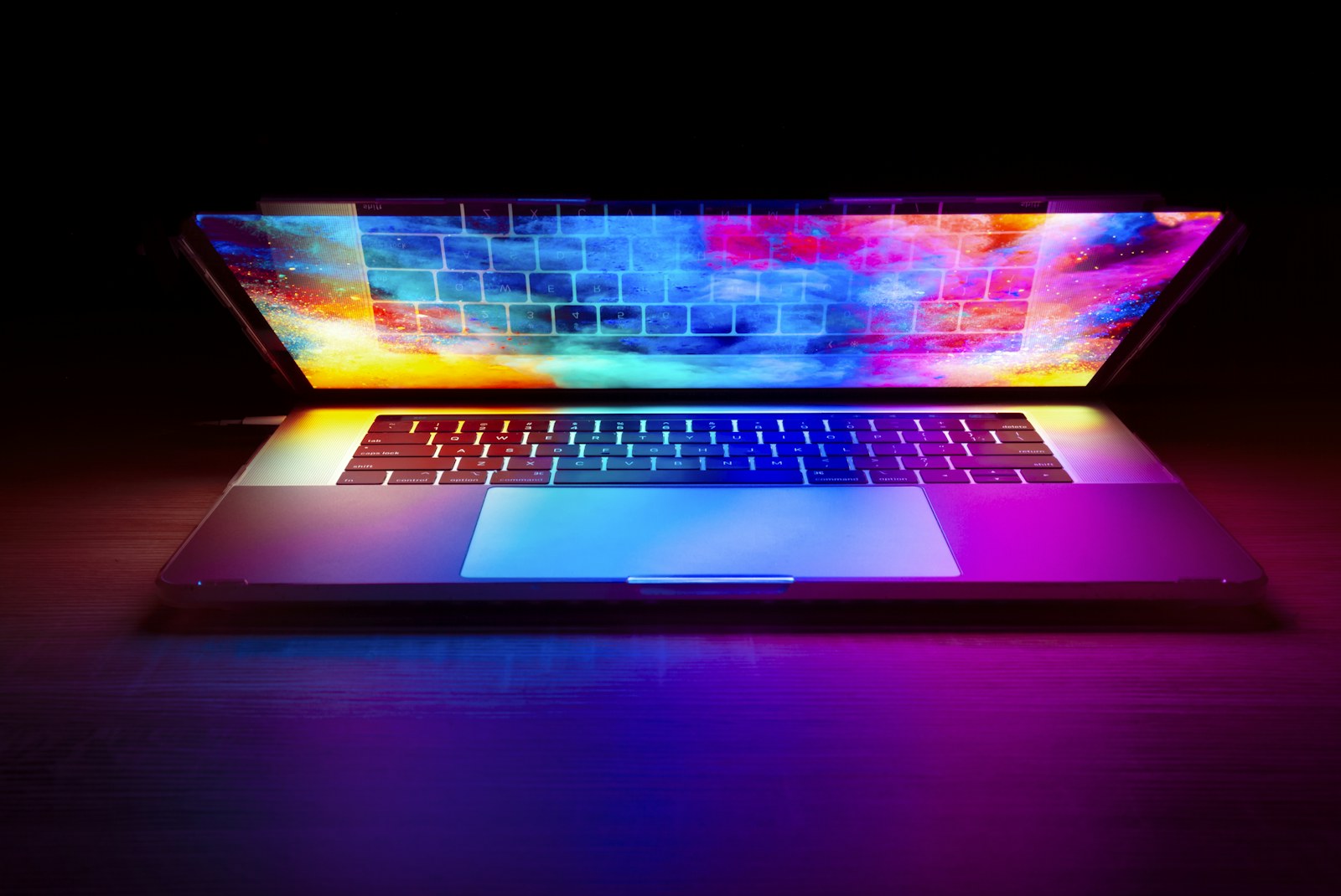 A laptop with a vibrant colorful screen glowing on a dark wooden desk