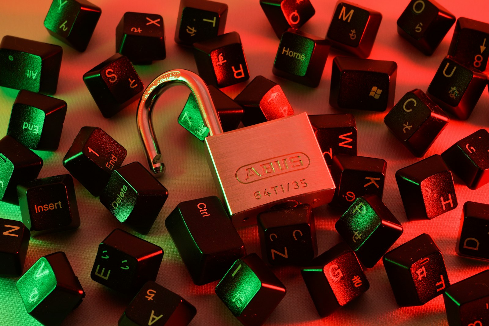 An open padlock surrounded by scattered black computer keyboard keys under red and green light