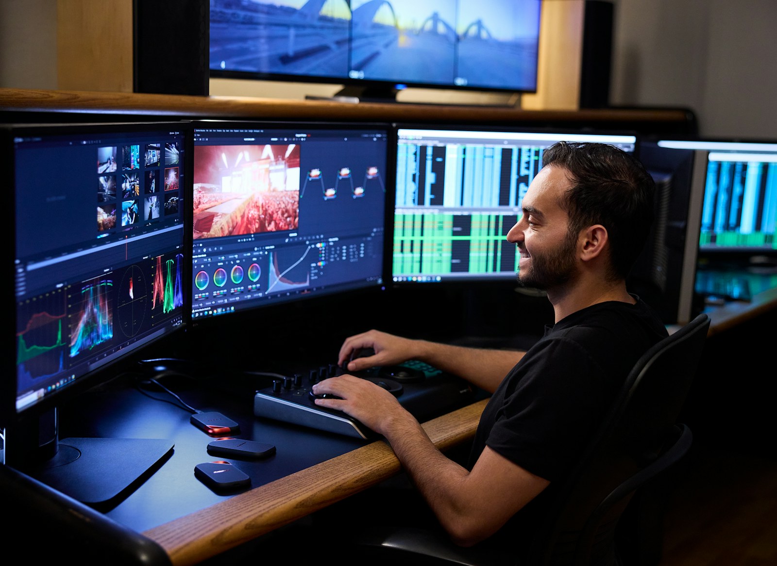 Smiling man editing video on multiple computer monitors