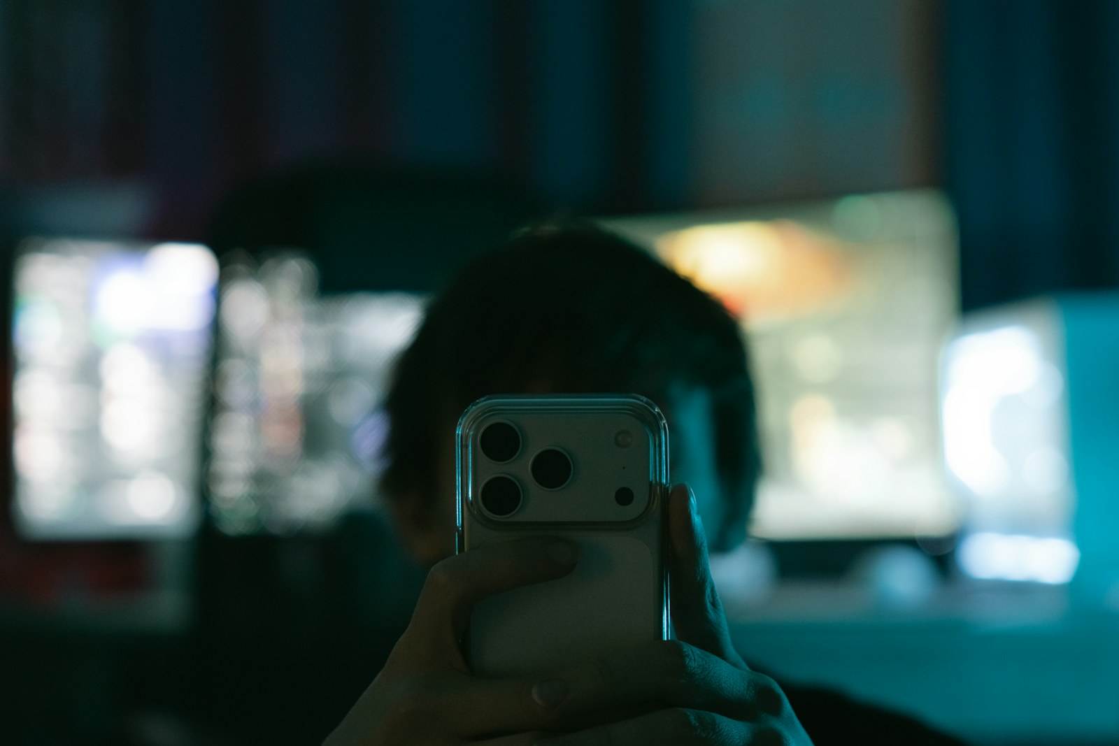 Person holding smartphone in front of multiple computer monitors