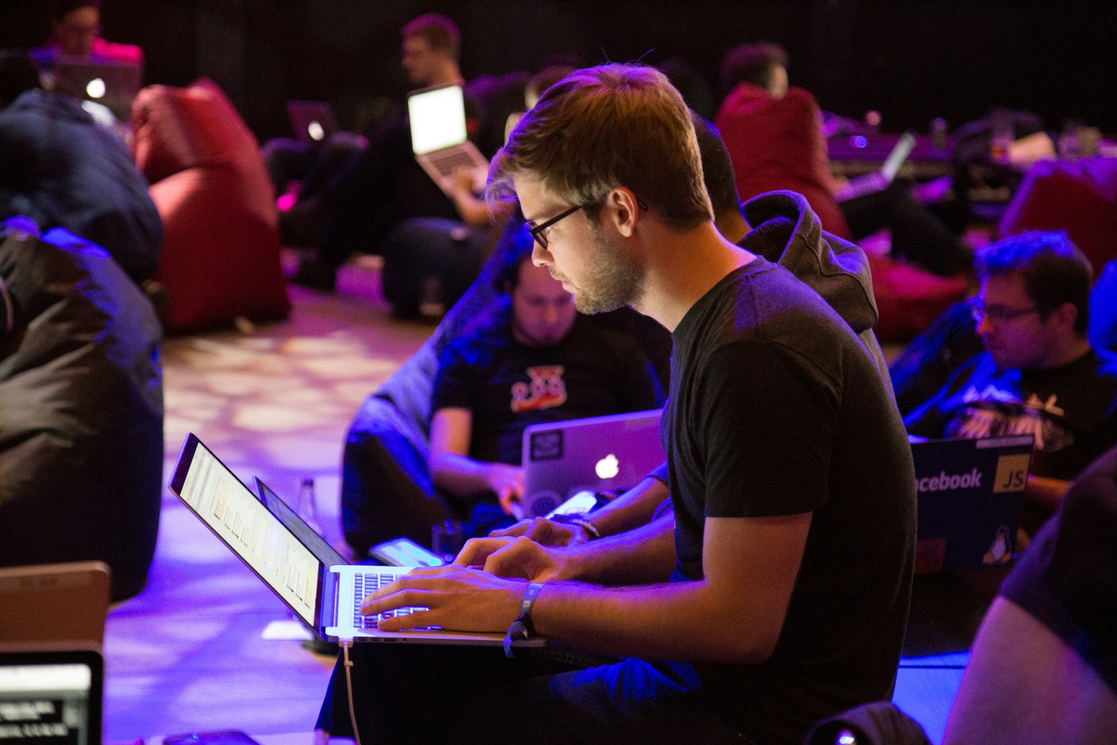 A man in glasses typing on a laptop in a dimly lit workspace
