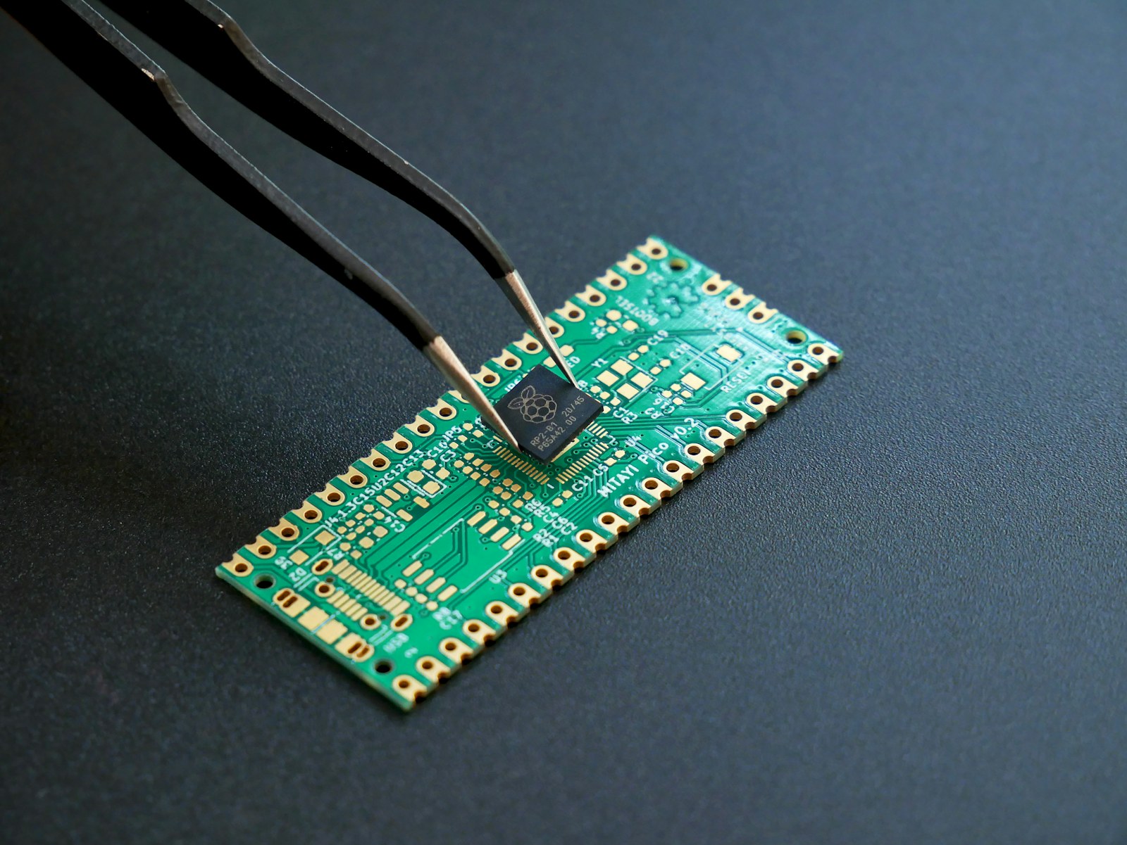 Tweezers placing a small black microchip onto a green circuit board