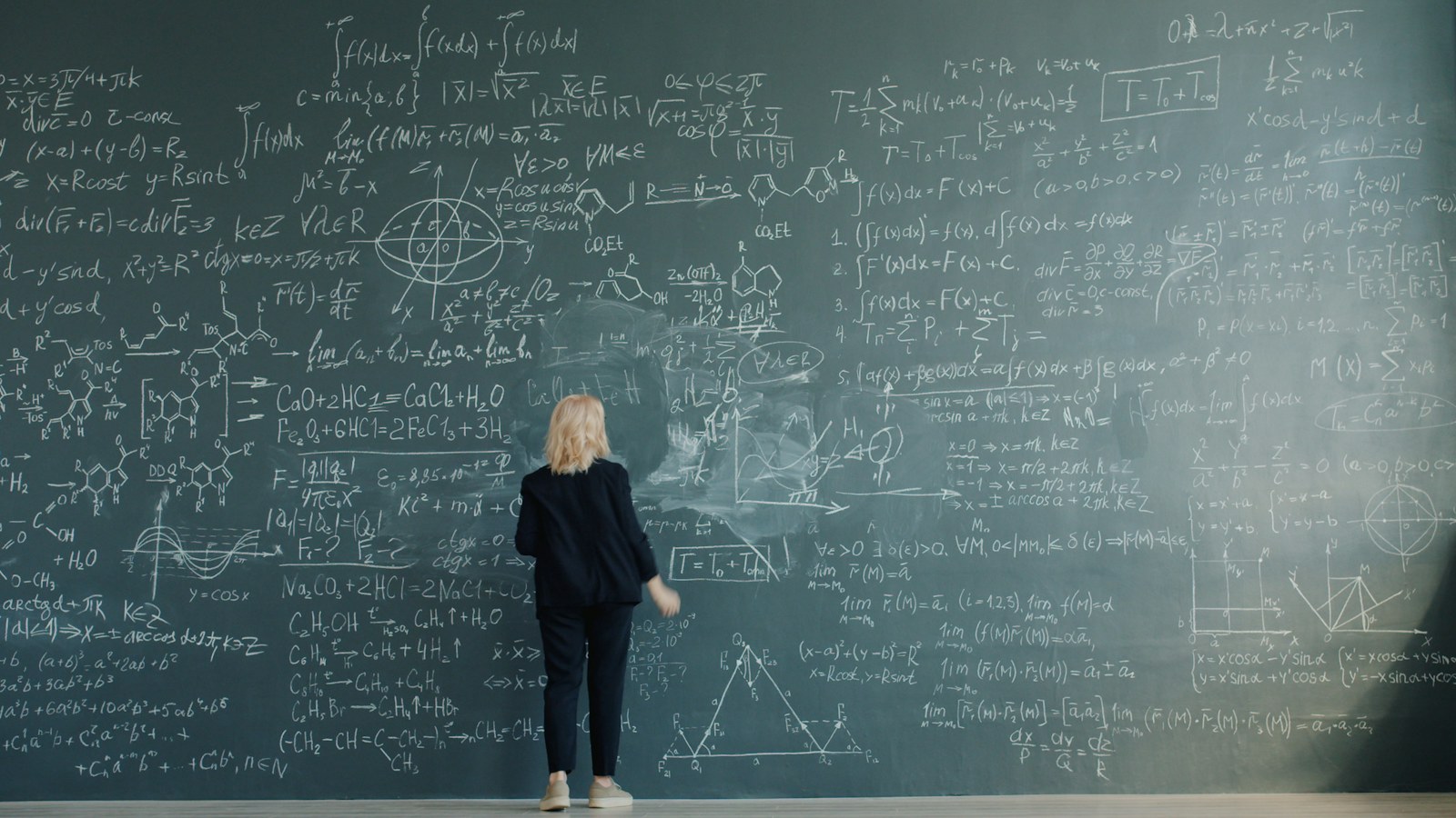 Woman writing complex formulas on a chalkboard wall